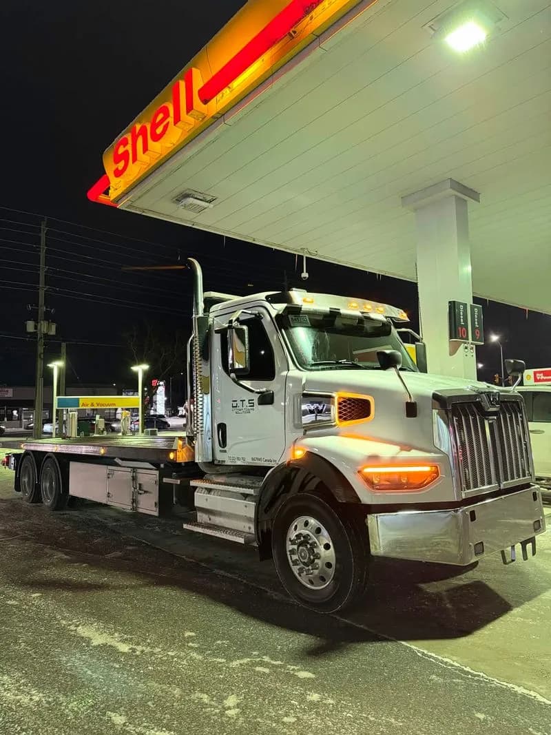 OTS flatbed tow truck parked at a gas station at night